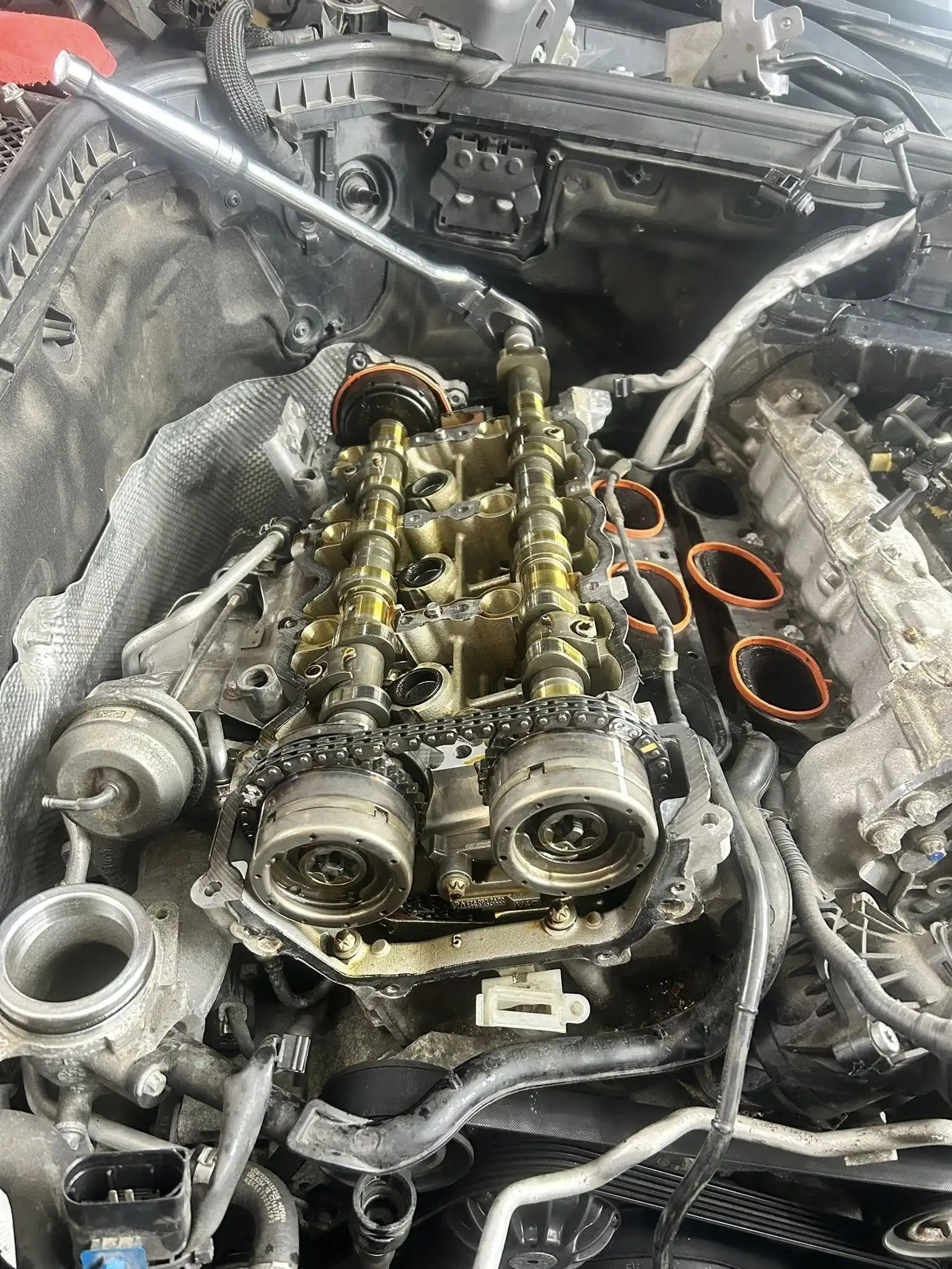 A close-up view of a car engine at Holland's Highline Automotive in MA, with the valve cover removed, exposing camshafts, timing chain, and internal components. Tools and engine parts are visible around the open engine bay at this expert engine repair shop.