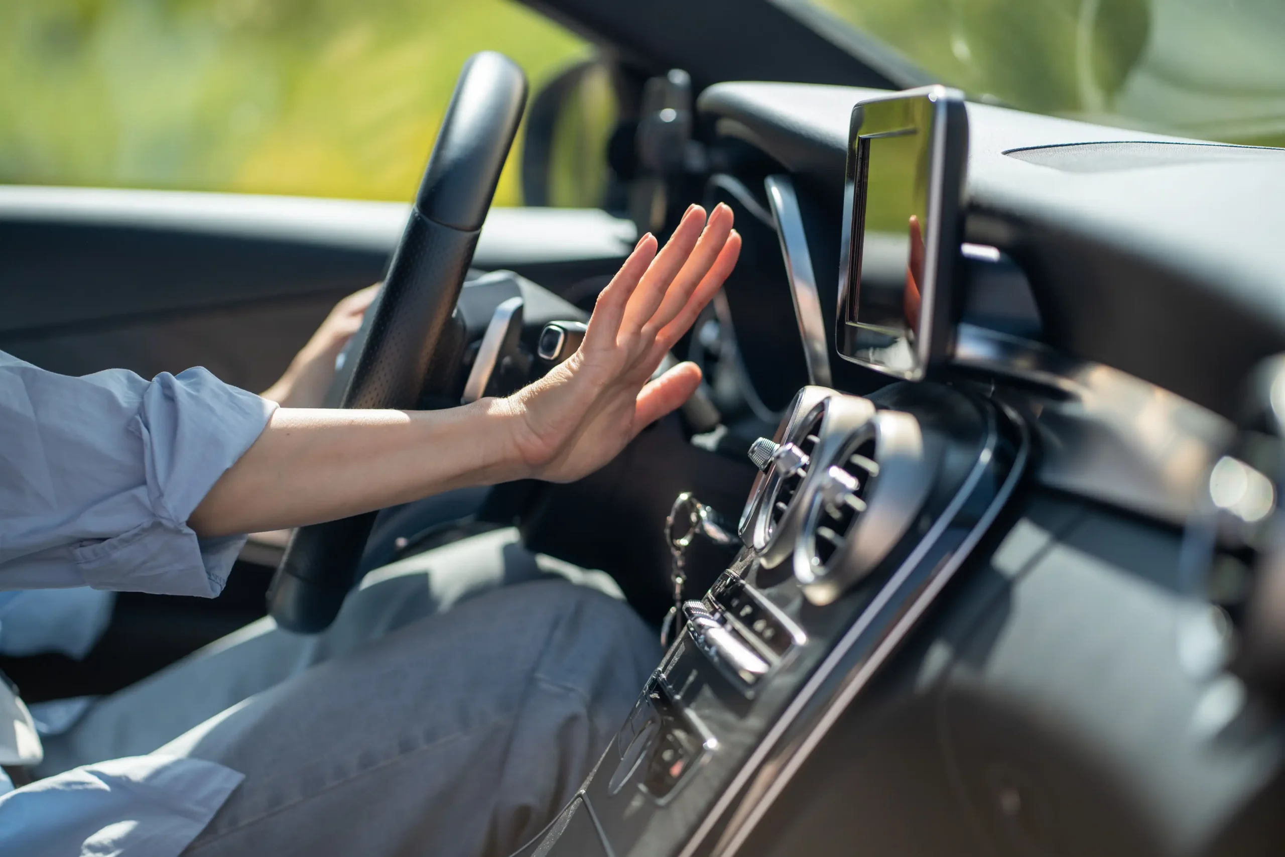 A person sitting in a car at Holland's Highline Automotive reaches for the touchscreen display on the dashboard, one hand on the wheel, highlighting the convenience offered by this trusted auto a/c repair shop.