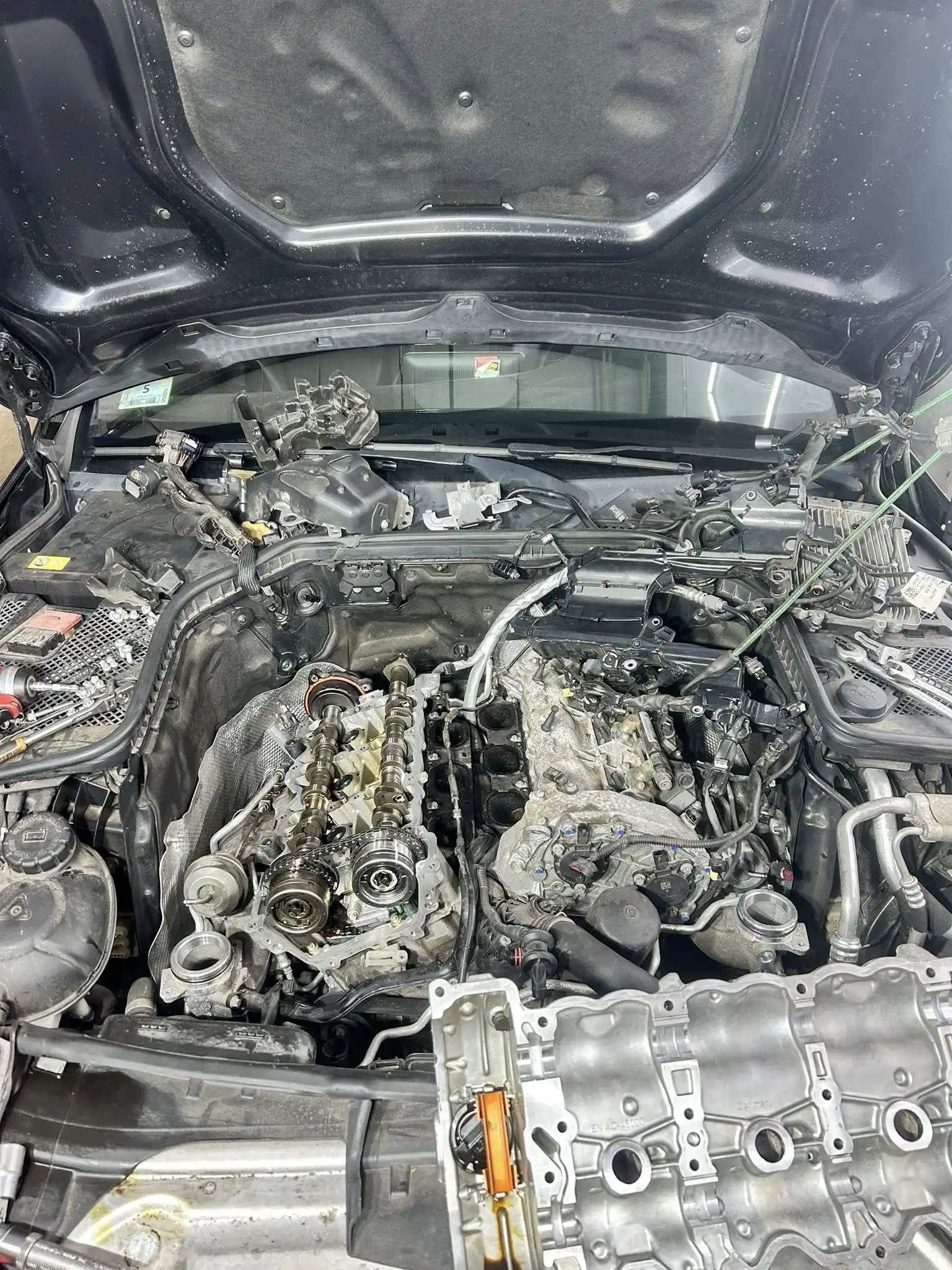 A car engine bay with the hood open at Holland's Highline Automotive in Bridgewater, showing a partially disassembled engine. Engine diagnostics and repair components are exposed, including the removed valve cover and parts laid out in the bay.