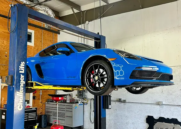 Porsche repair in Bridgewater, MA at Holland’s Highline Automotive. A blue sports car is lifted on a hydraulic car lift inside Holland's Highline Automotive, a top choice for Porsche repair in Bridgewater, MA, with garage tools and equipment visible in the background.