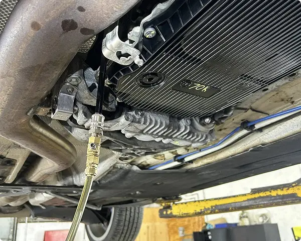 Transmission repair and replacement in Bridgewater, MA at Holland’s Highline Automotive. A close-up view of a car’s undercarriage showing an automatic transmission fluid change in progress, with a hose connected to the transmission pan—part of expert automatic transmission repair Bridgewater drivers trust.