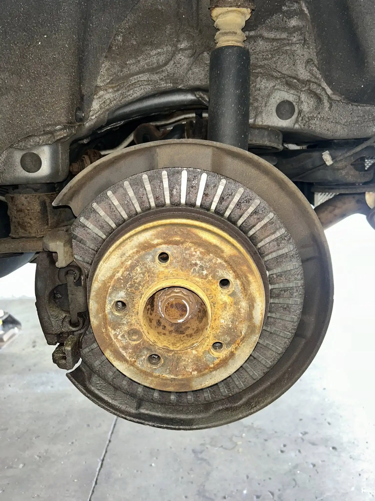Close-up of a car wheel hub and brake rotor with visible rust and wear, viewed from the side at Holland's Highline Automotive. The brake caliper is attached on the left, highlighting the need for professional brake repair Bridgewater drivers trust.