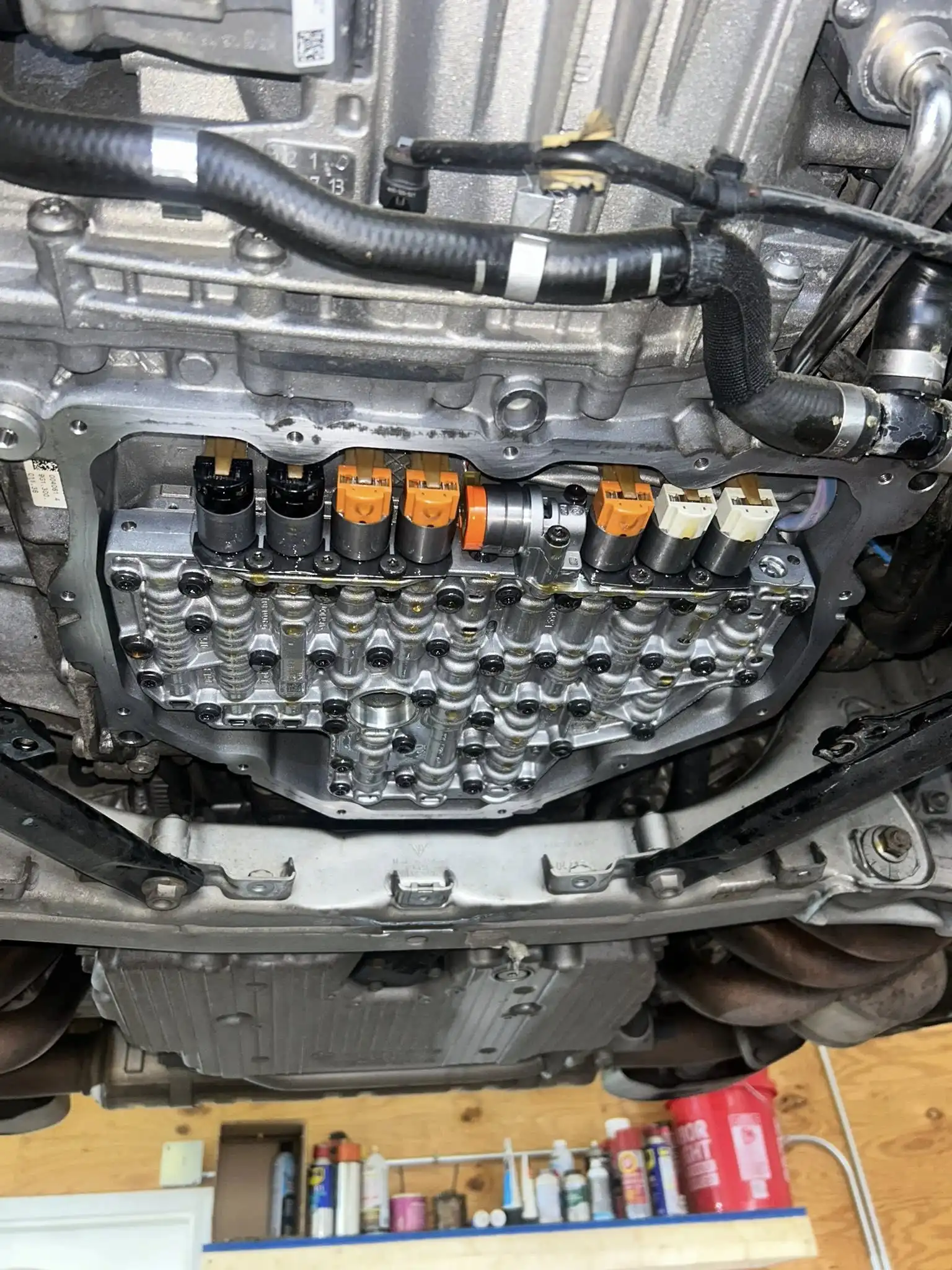 Close-up view of the underside of a car showing the exposed automatic transmission valve body with several solenoids in different colors, surrounded by metal components and wiring.