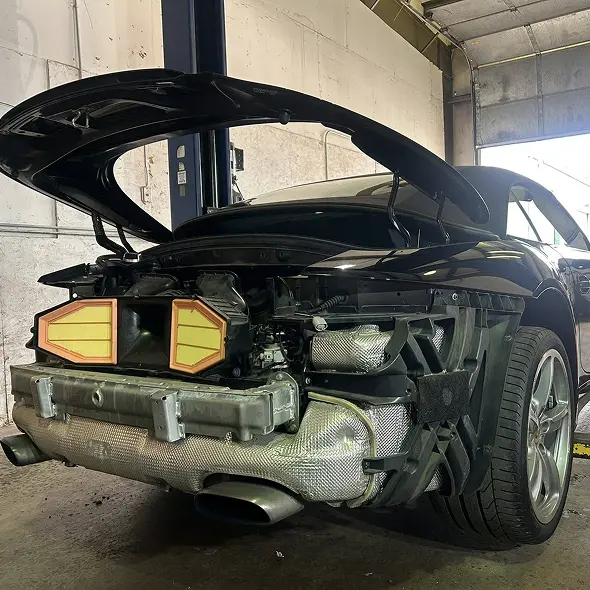 A black car with its rear bumper removed and engine exposed, parked inside Holland's Highline Automotive in MA for Porsche repair Bridgewater, showcasing internal components and wiring with the rear trunk open.