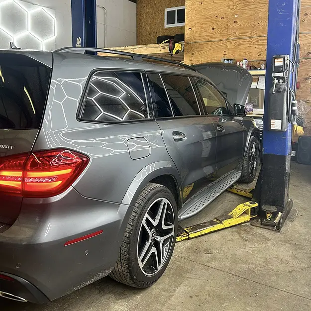 A grey SUV with its hood open is parked inside Holland's Highline Automotive, an auto repair shop in MA, positioned on a hydraulic lift with bright lights reflecting off its surface—your local choice for Mercedes repair Bridgewater.