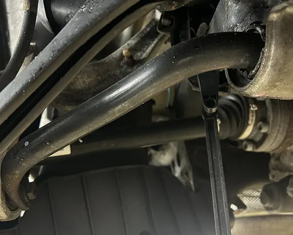 Suspension repair in Bridgewater, MA at Holland’s Highline Automotive. Close-up view of a car’s suspension system with metal rods, joints, a zip tie on the sway bar, and a rubber boot on the CV axle shaft—showing some dirt and use. Suspension repair Bridgewater, MA by Holland's Highline Automotive.