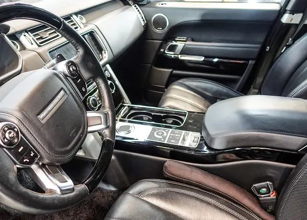 Interior view of a modern car showing leather seats, steering wheel, center console with controls and cup holders, and the dashboard with air vents and touchscreen display at Holland's Highline Automotive, your MA Land Rover repair experts in Bridgewater.