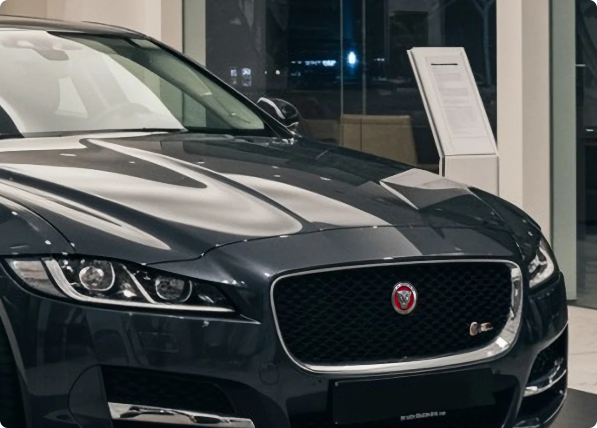 A close-up of a dark gray Jaguar car on display in a showroom, showing the front grille with the Jaguar logo, sleek headlights, and part of the hood—highlighting expert jaguar service for your European vehicle under bright indoor lighting.