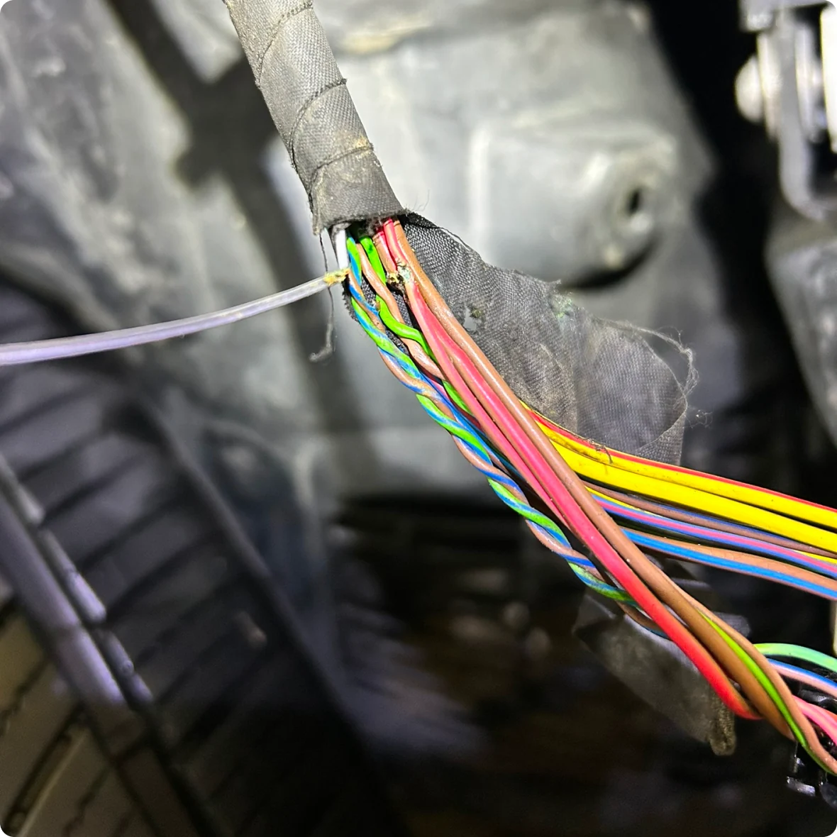 Close-up of exposed and frayed electrical wires wrapped in black tape, showing various colored wires inside a European vehicle during auto electrical repair.